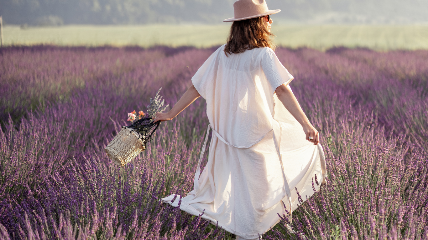 Woman in a white dress and hat walking through a lavender field.